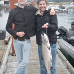 Two men in black jackets and a man holding fish